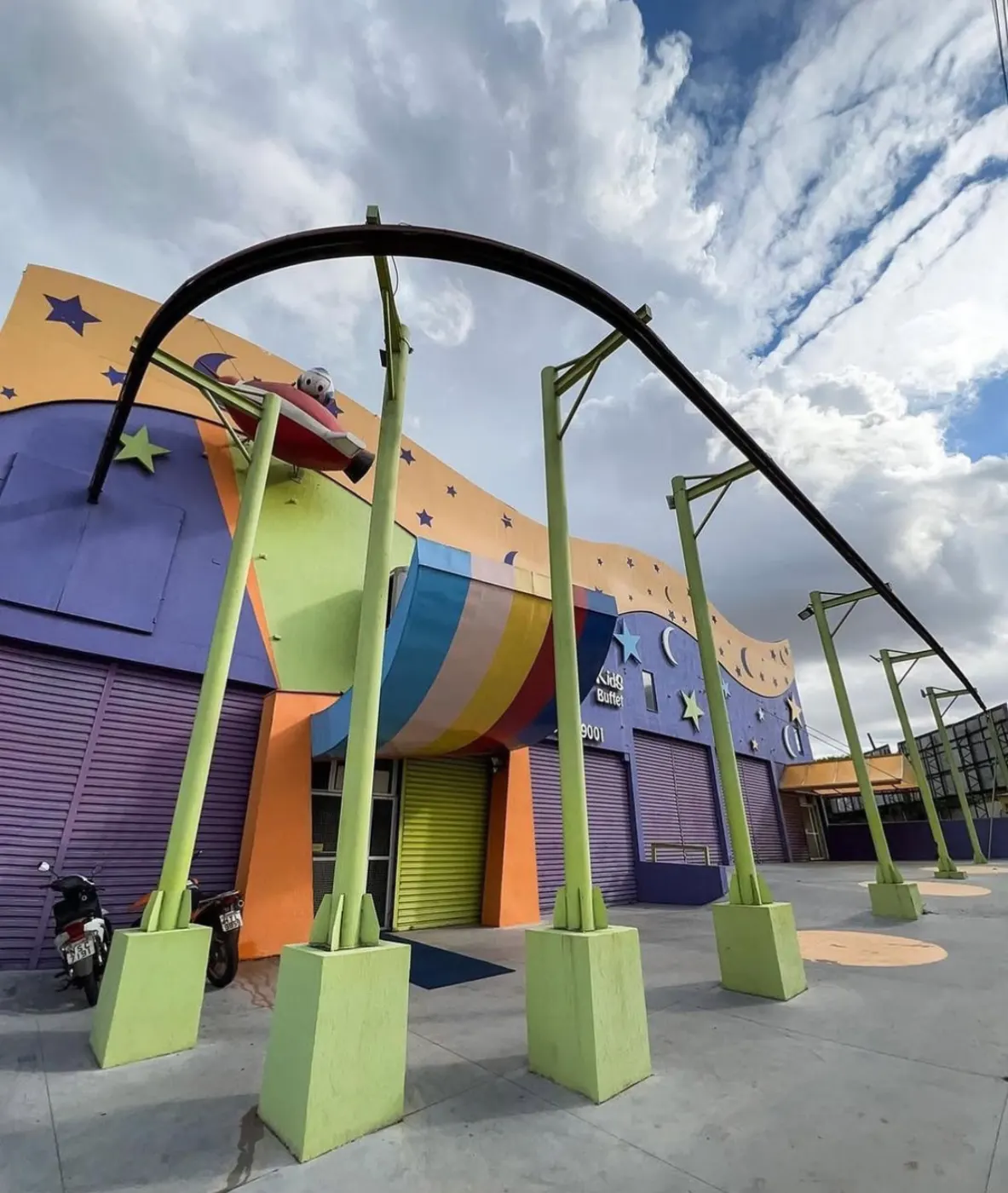 Fachada do Planeta Eventos: prédio colorido com estrelas e luas pintadas, arcos que passam por cima da entrada e a escultura de um disco voador