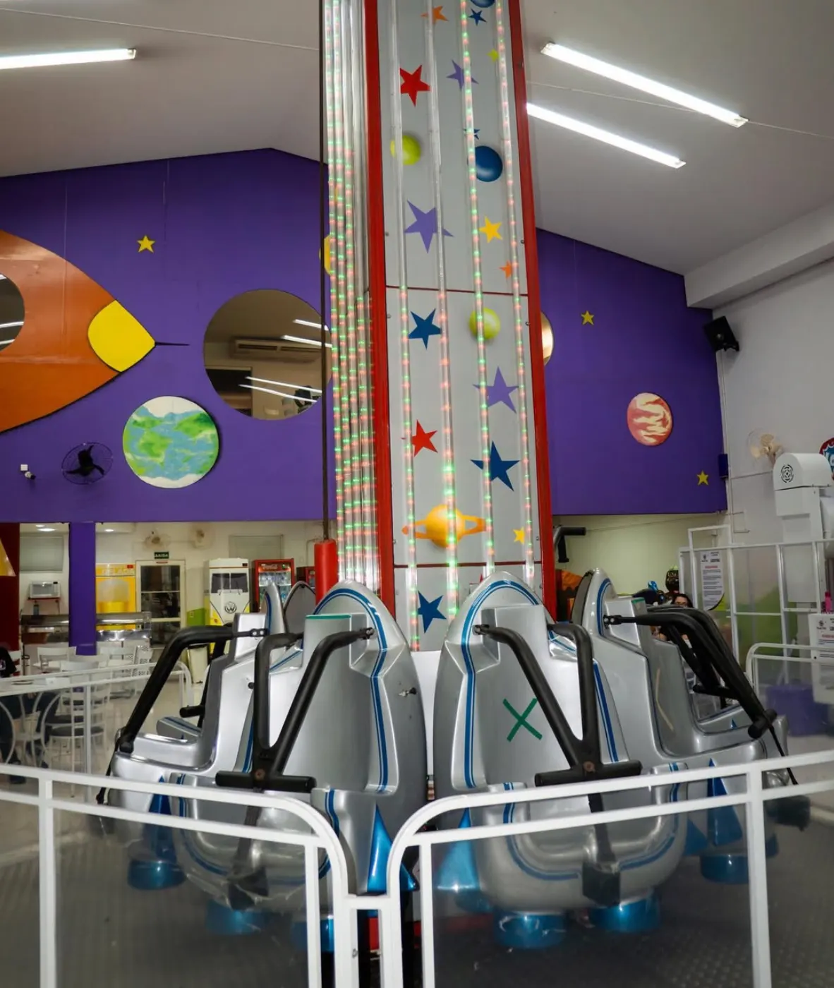 Torre de queda infantil com coluna de luzes de LED, diante de um mural espacial com foguete, planetas e estrelas